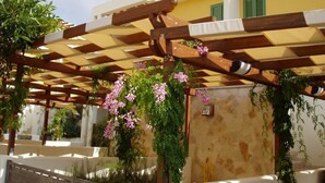 Un área de estar al aire libre con techo, vigas de madera y plantas en macetas.