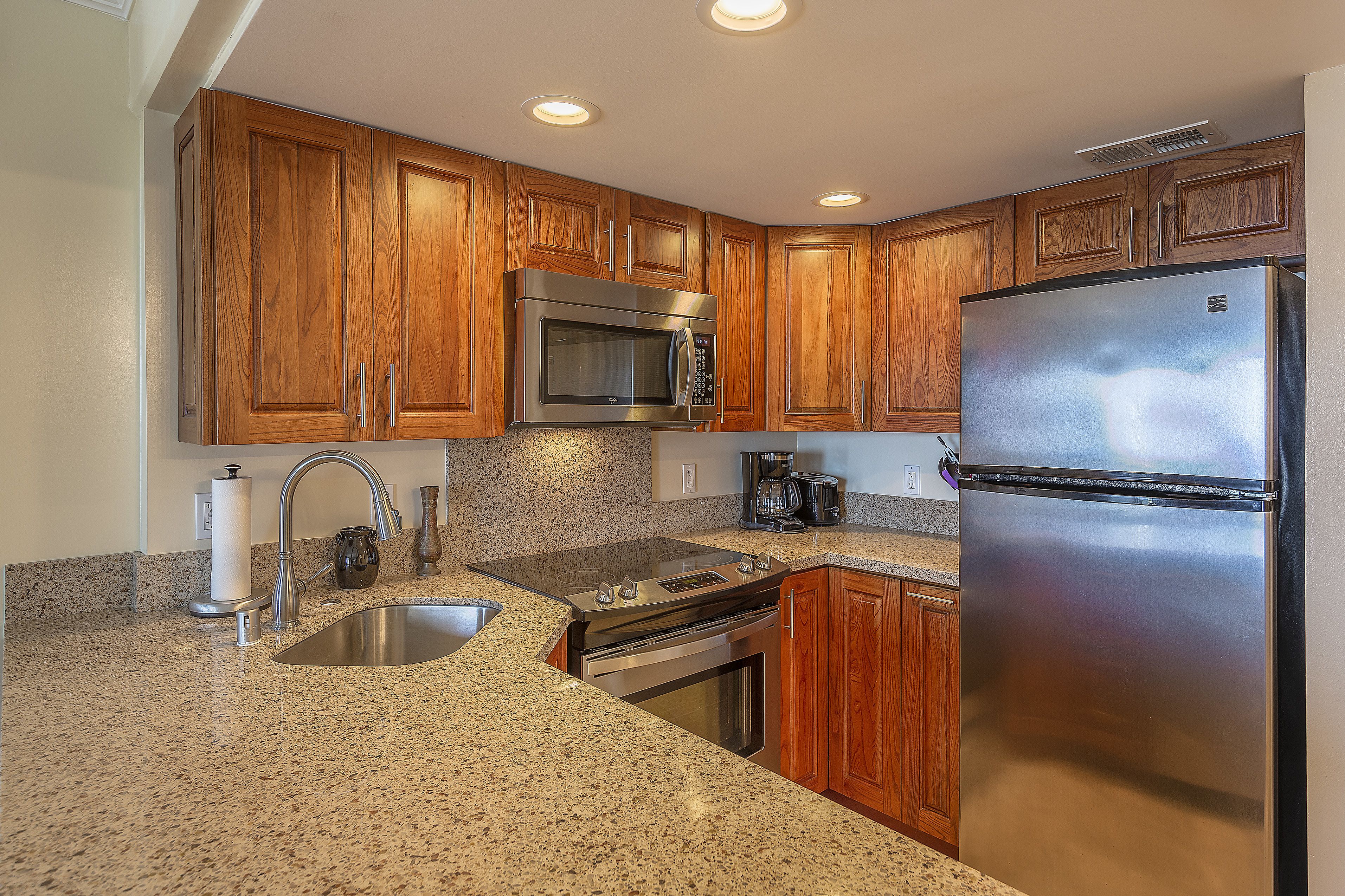 A kitchen with wooden cabinets, stainless steel appliances, granite countertops, and a stainless steel refrigerator.
