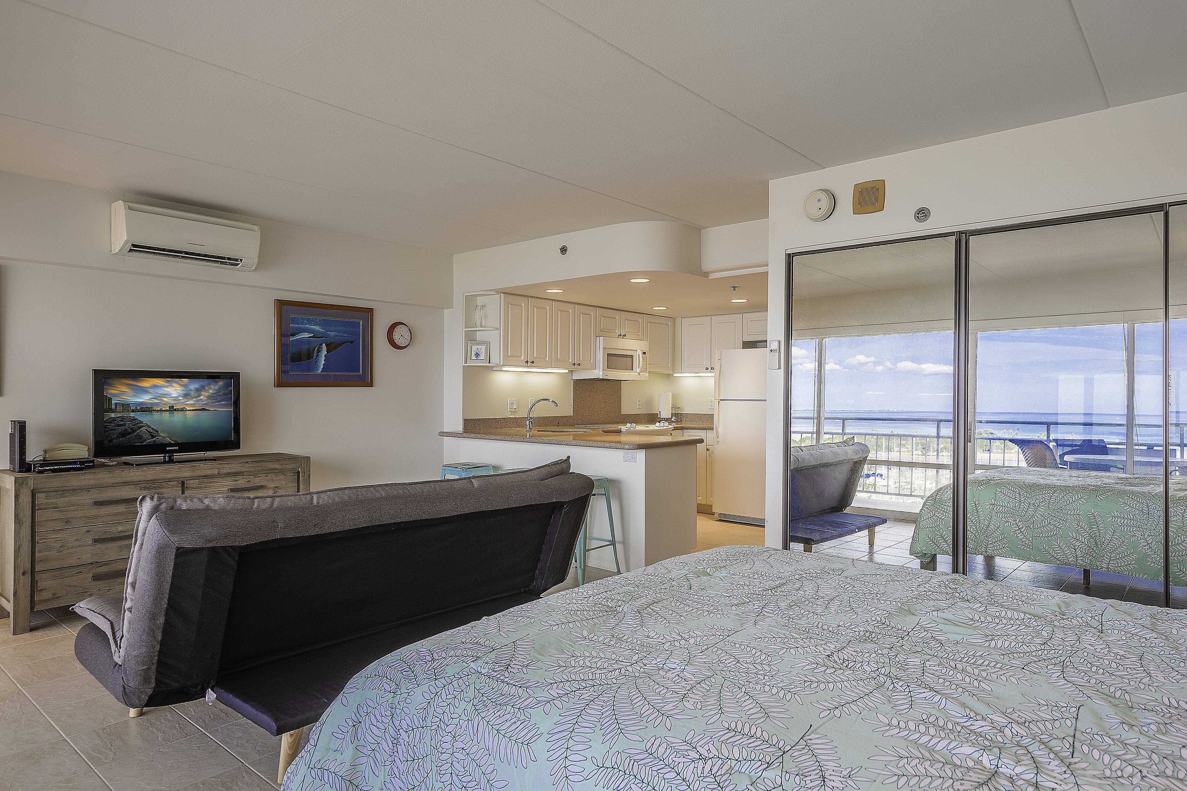 A bedroom with a bed, a sofa, a TV, and a view of the balcony.