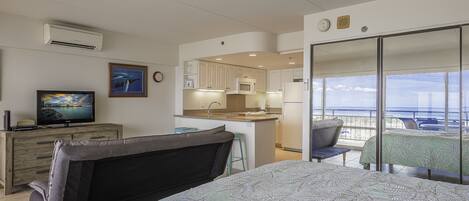 A bedroom with a bed, a sofa, a TV, and a view of the balcony.