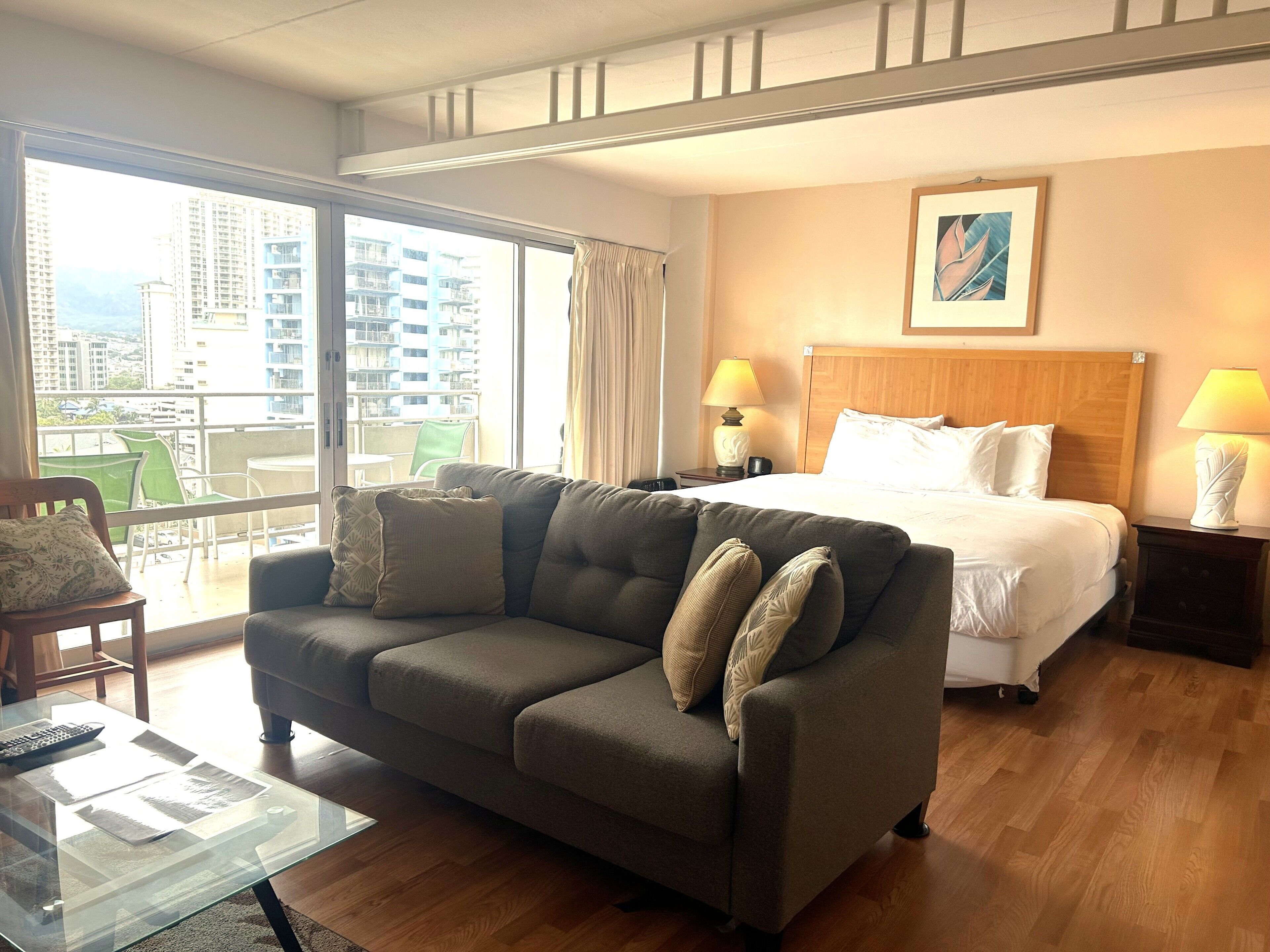 Habitación de hotel con cama, sofá, una mesa de centro de vidrio y vista a la ciudad.