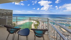 A balcony with wicker chairs and a table, overlooking a beach and marina with boats. - Ilikai by Luana Hawaii Vacation Rentals (Honolulu)