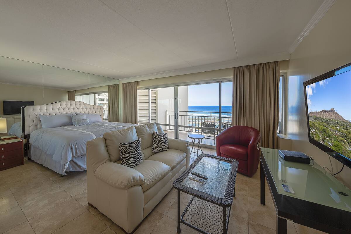 A hotel room with a bed, a sofa, a desk, and a view of the ocean.