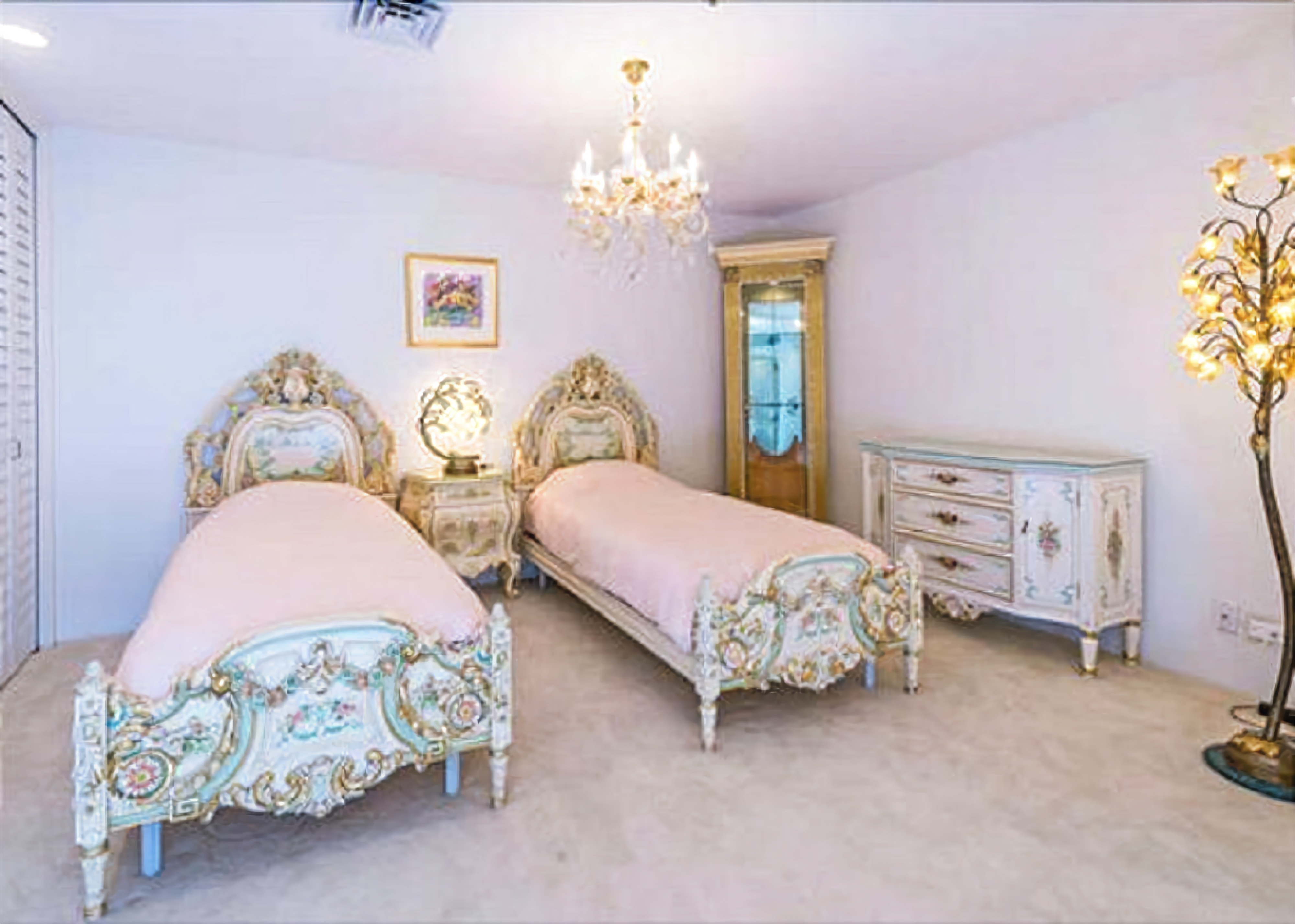 A bedroom with two ornate beds, a chandelier, a dresser, and a mirror.