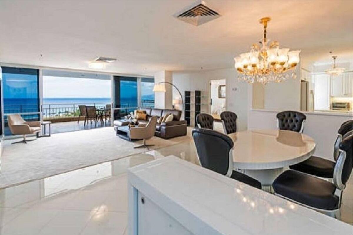 A spacious living area with a dining table and chairs, a chandelier, and a view of the ocean.