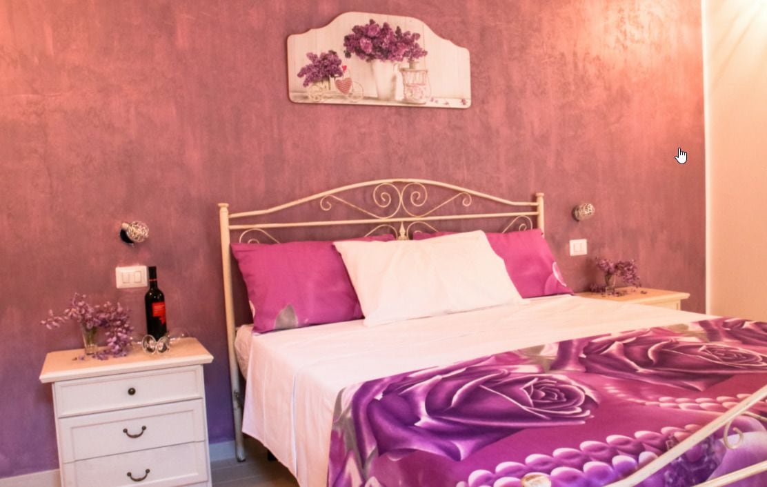 A bedroom with a bed, a nightstand, a wall-mounted decoration, and a bedside table with a bottle and flowers.