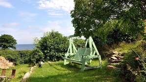 A green swing chair in a grassy area with a view of the sea. - Danchelshus (Allinge)