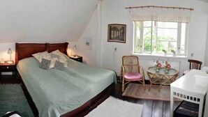A bedroom with a bed, bedside tables, a window with a view, a chair, a small table, and a white cabinet. - Danchelshus (Allinge)