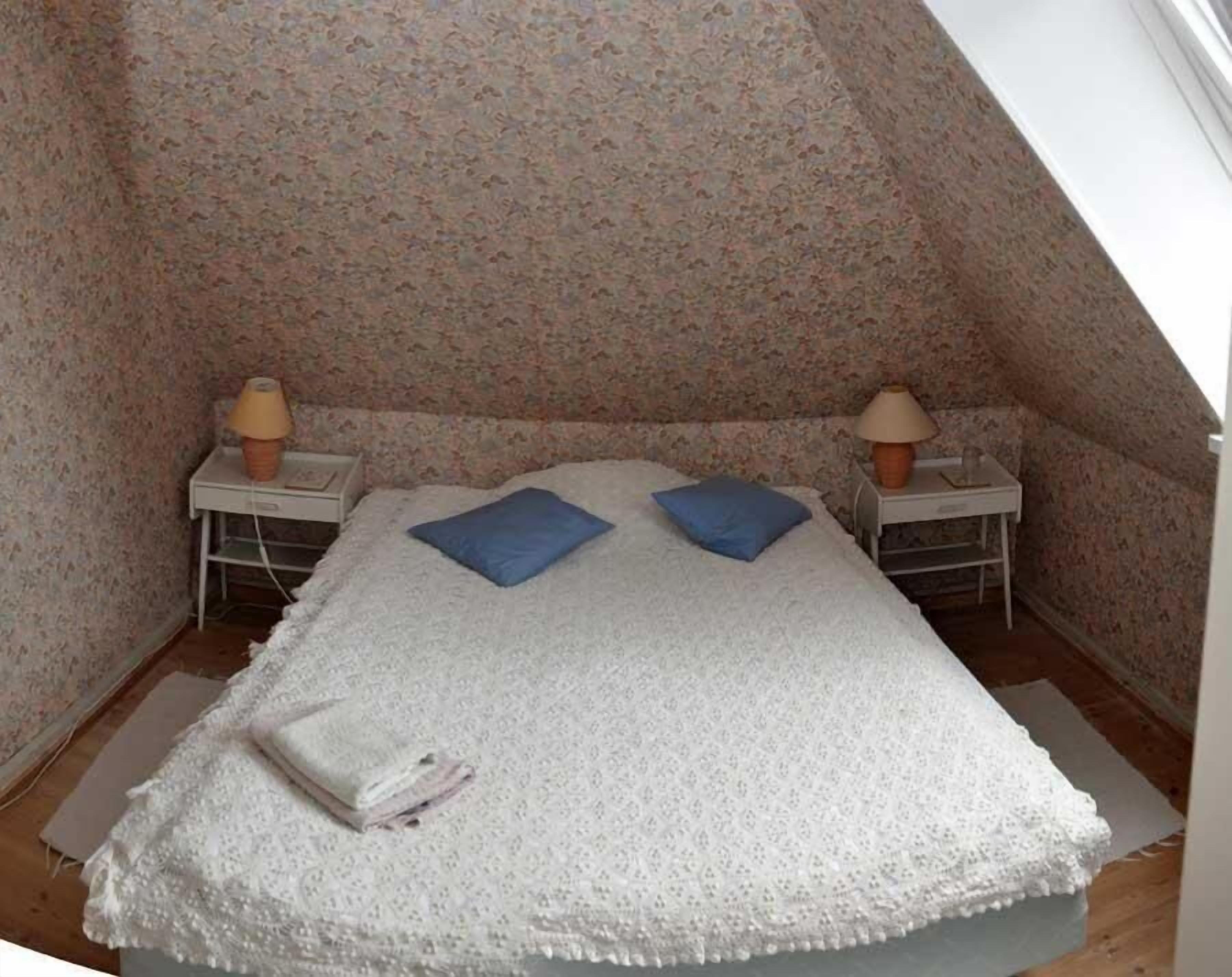 A small, cozy room with a bed, two nightstands, and two lamps.