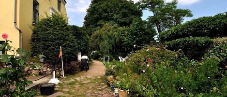 A garden pathway leading to a building with a yellow facade, surrounded by various potted plants and flowers.