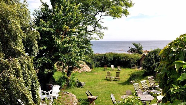 A garden with outdoor seating, a view of the sea, and lush greenery. - Danchelshus (Allinge)