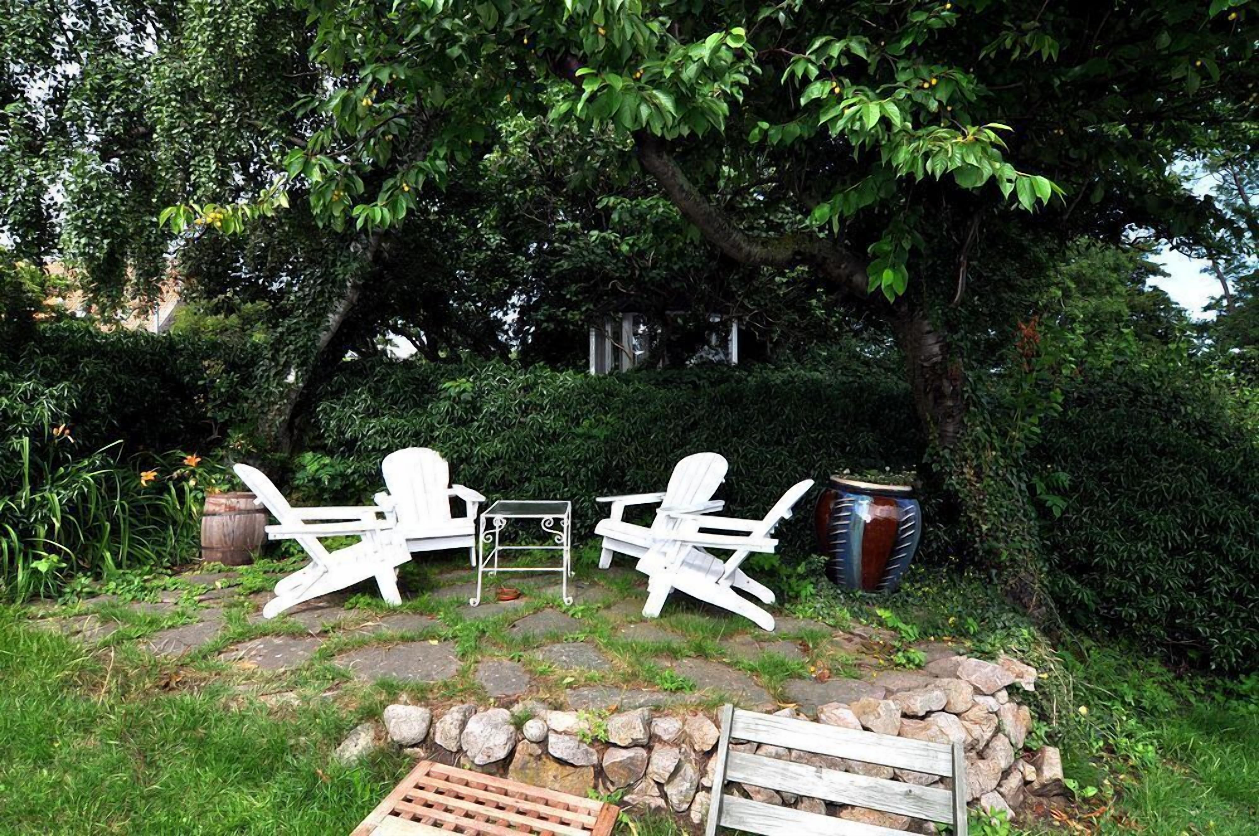 A garden with two white Adirondack chairs, a metal table, and a stone wall.