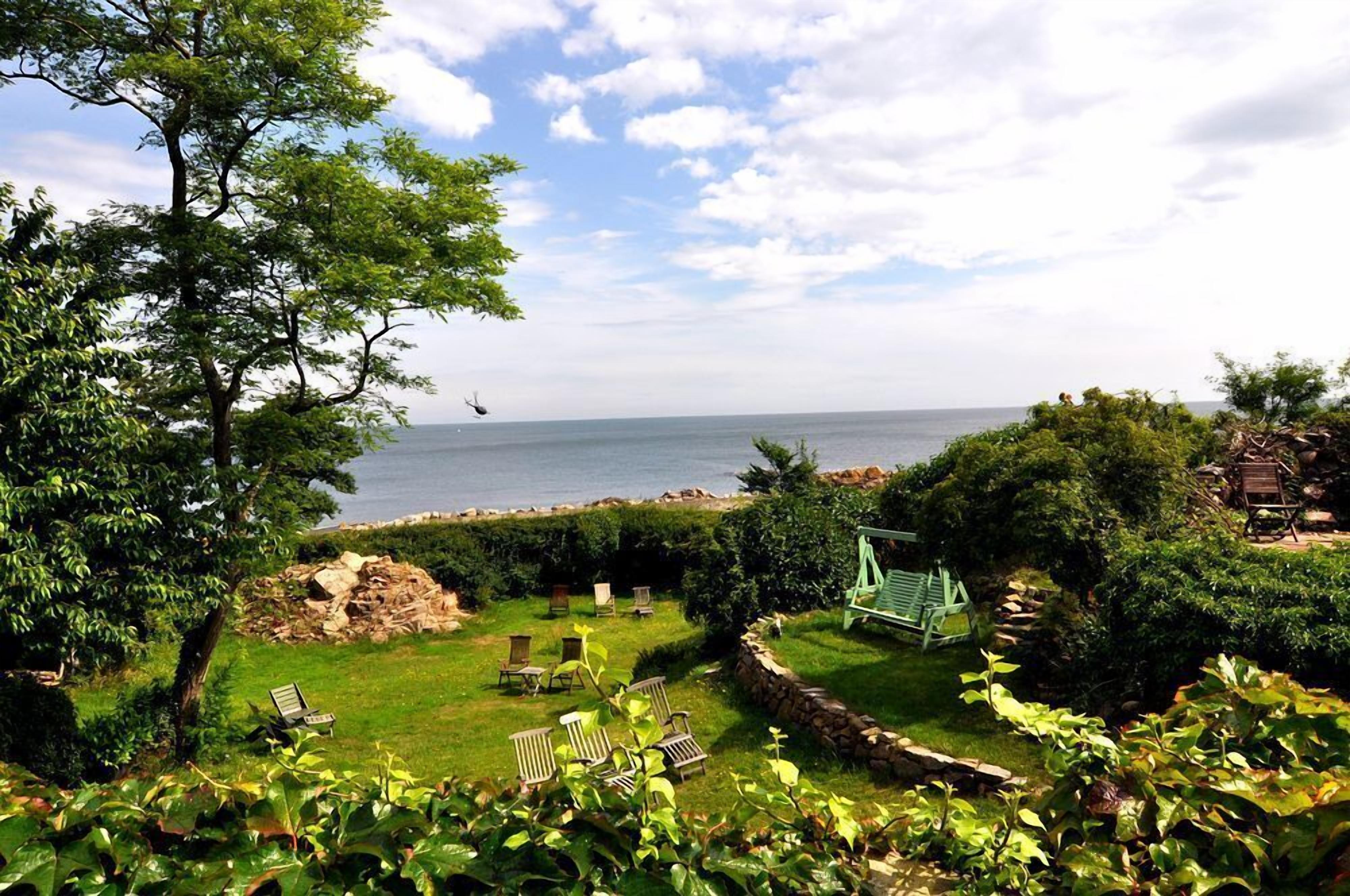 A garden with a swing set, chairs, and a view of the sea.