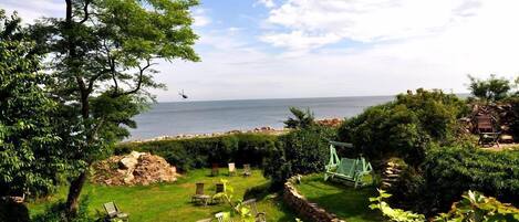 Um jardim com baloiço, cadeiras e vista para o mar.