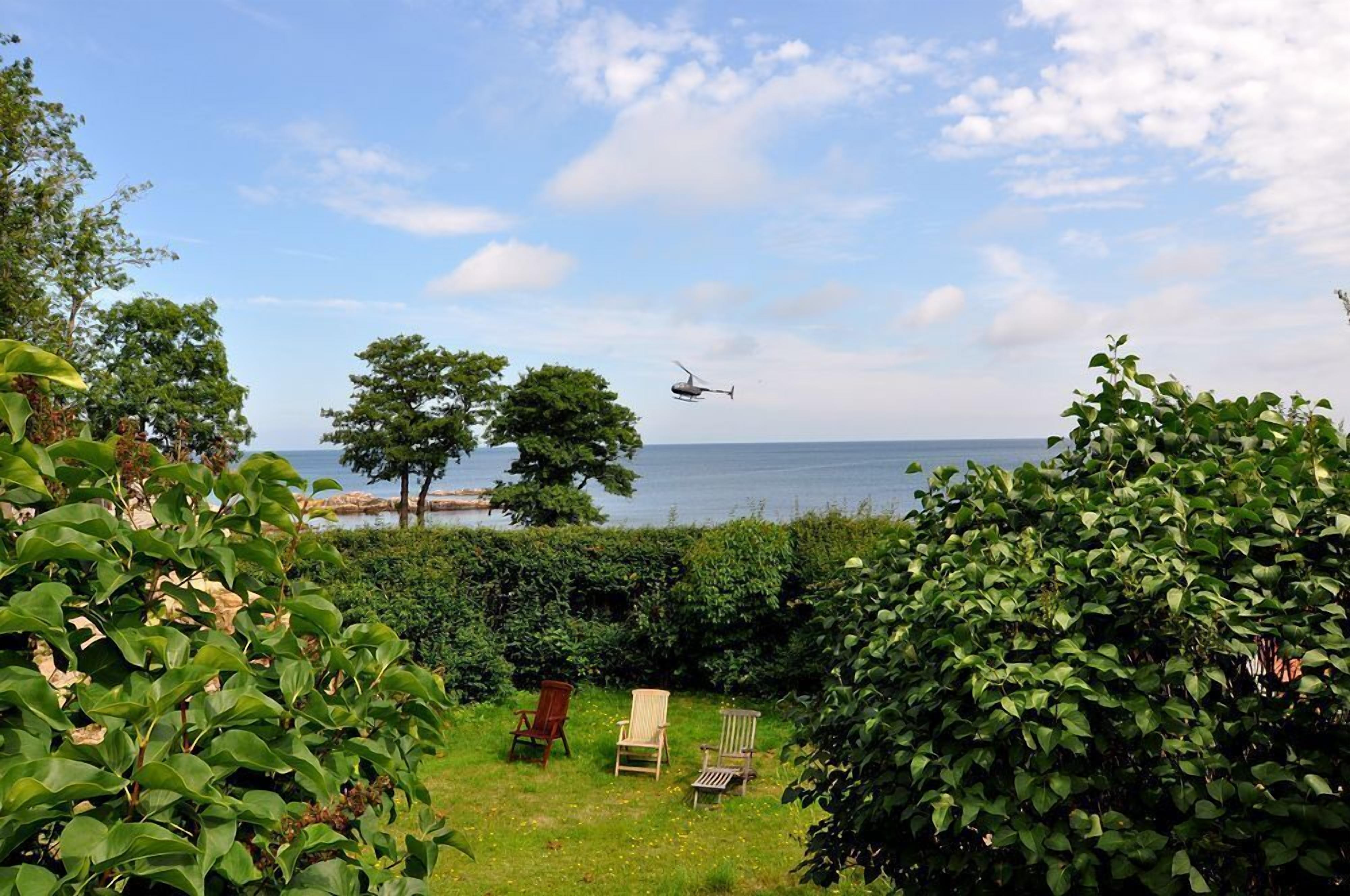 A garden with a view of the sea and a helicopter in the sky.