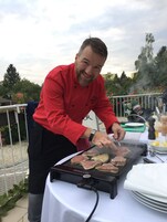 A person grilling meat outdoors with a table set up nearby.