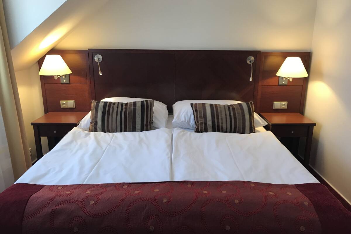 A double bed with white linens, two striped pillows, a dark headboard, and bedside lamps.