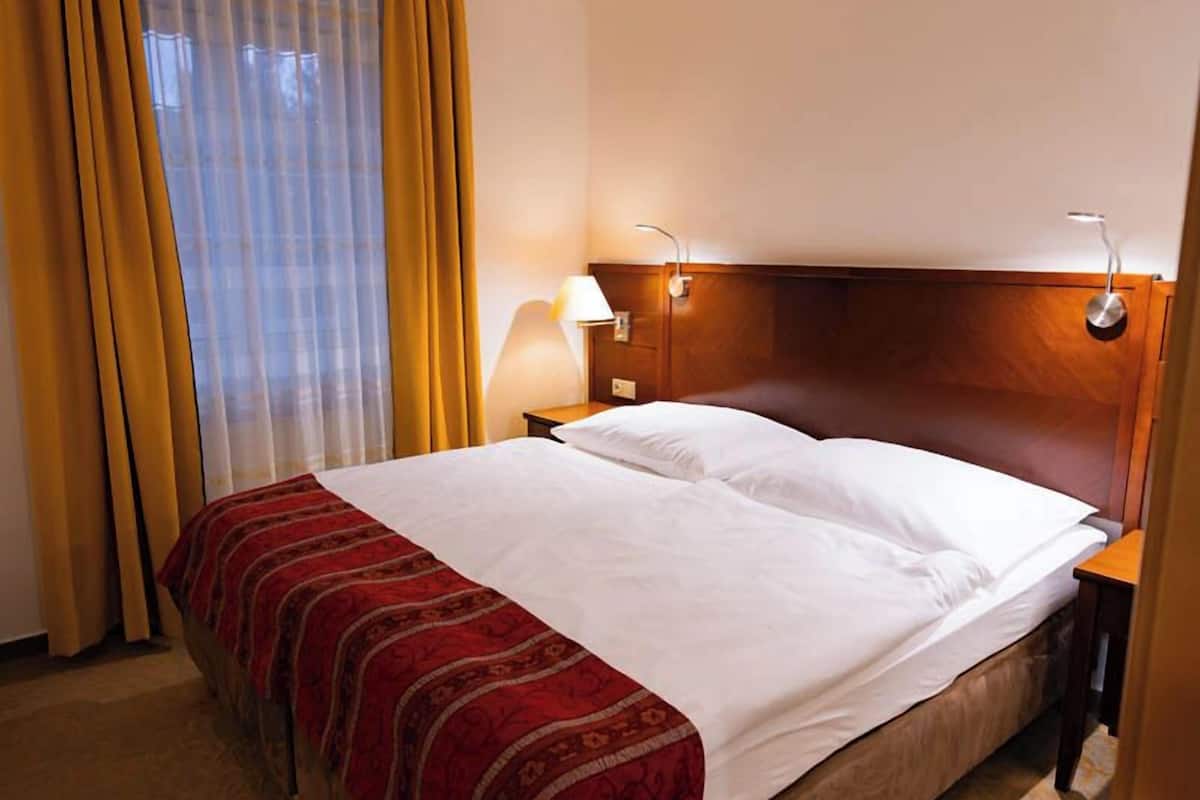 A hotel room with a bed, a nightstand, a lamp, and a window with curtains.