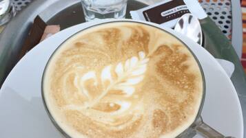 A cup of coffee with latte art on a white plate, placed on a tray with a glass of water, a wallet, and a mobile phone.