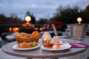 A table set with plates of food, a basket of bread, a vase with flowers, and a candle.
