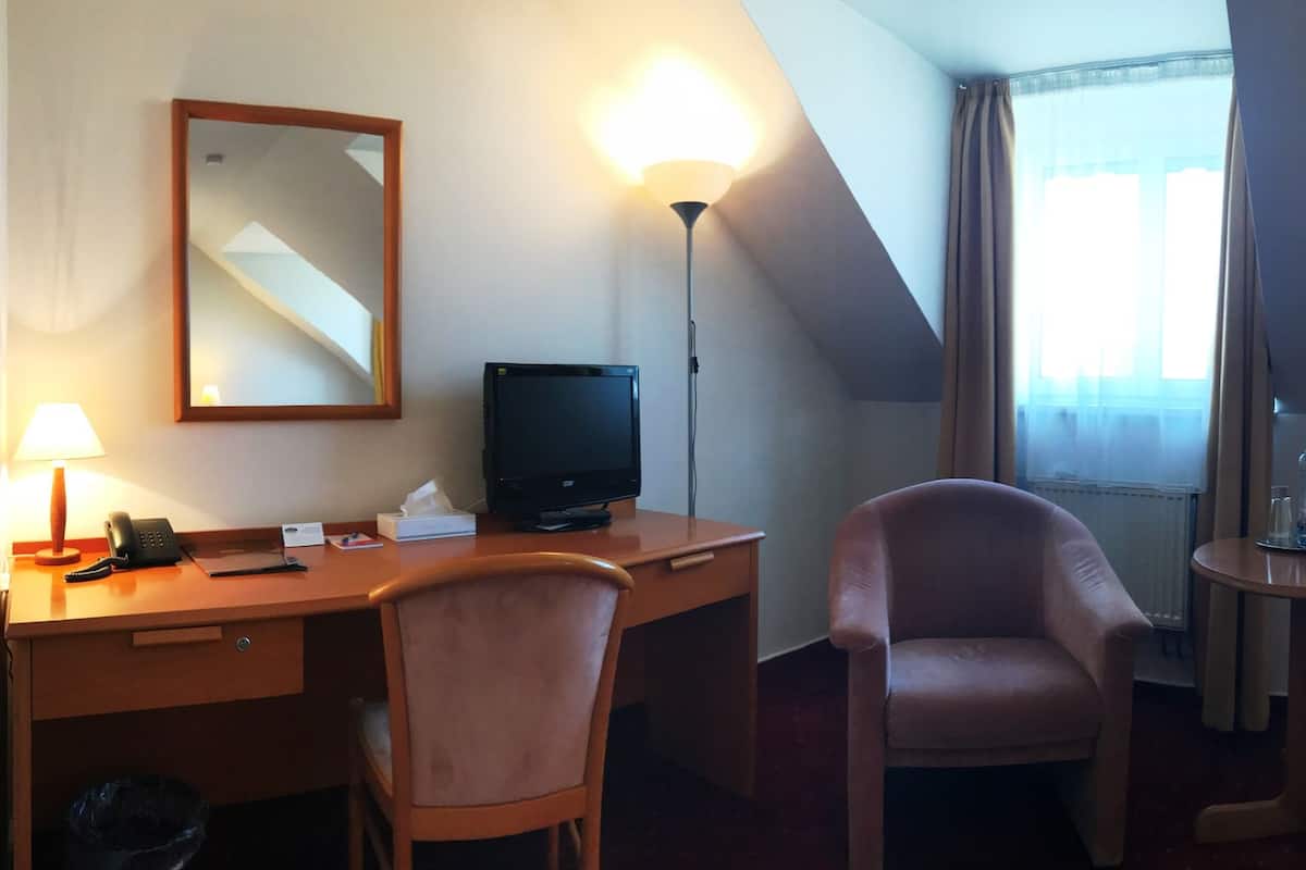 A hotel room with a desk, chair, two beds, a small table, and a mirror.