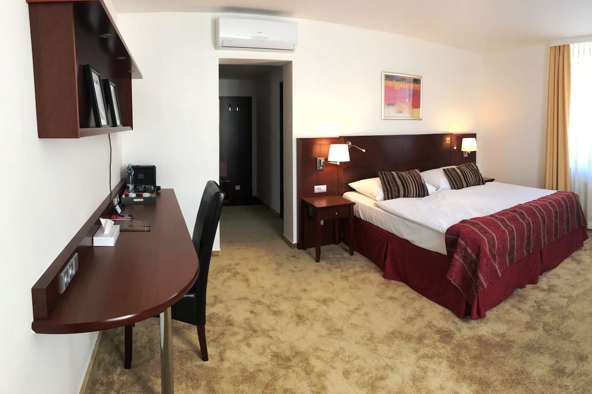 A hotel room with a bed, desk, chair, and a small table.