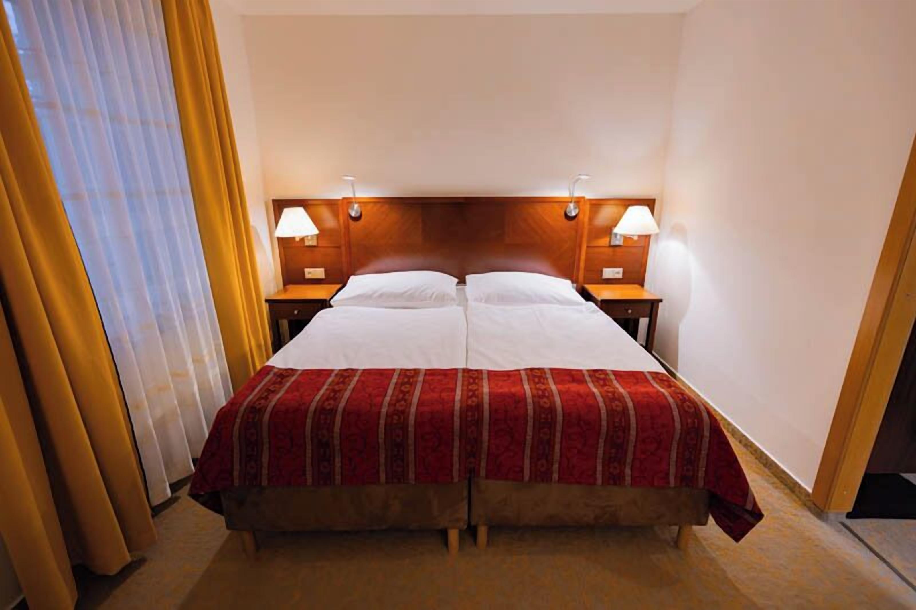 Una cama doble con colcha roja y blanca, dos mesitas de noche con lámparas y un cabecero de madera.