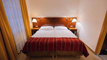 Una cama doble con colcha roja y blanca, dos mesitas de noche con lámparas y un cabecero de madera.