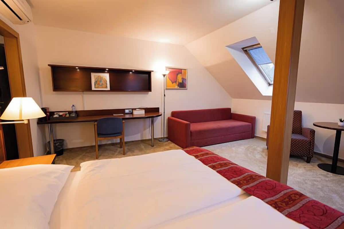 A hotel room with a bed, desk, chair, red sofa, and a small table.