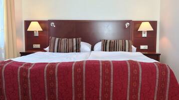 Un lit double avec une couvre-lit à motifs rouges et beiges, deux lampes de chevet et deux coussins à rayures.