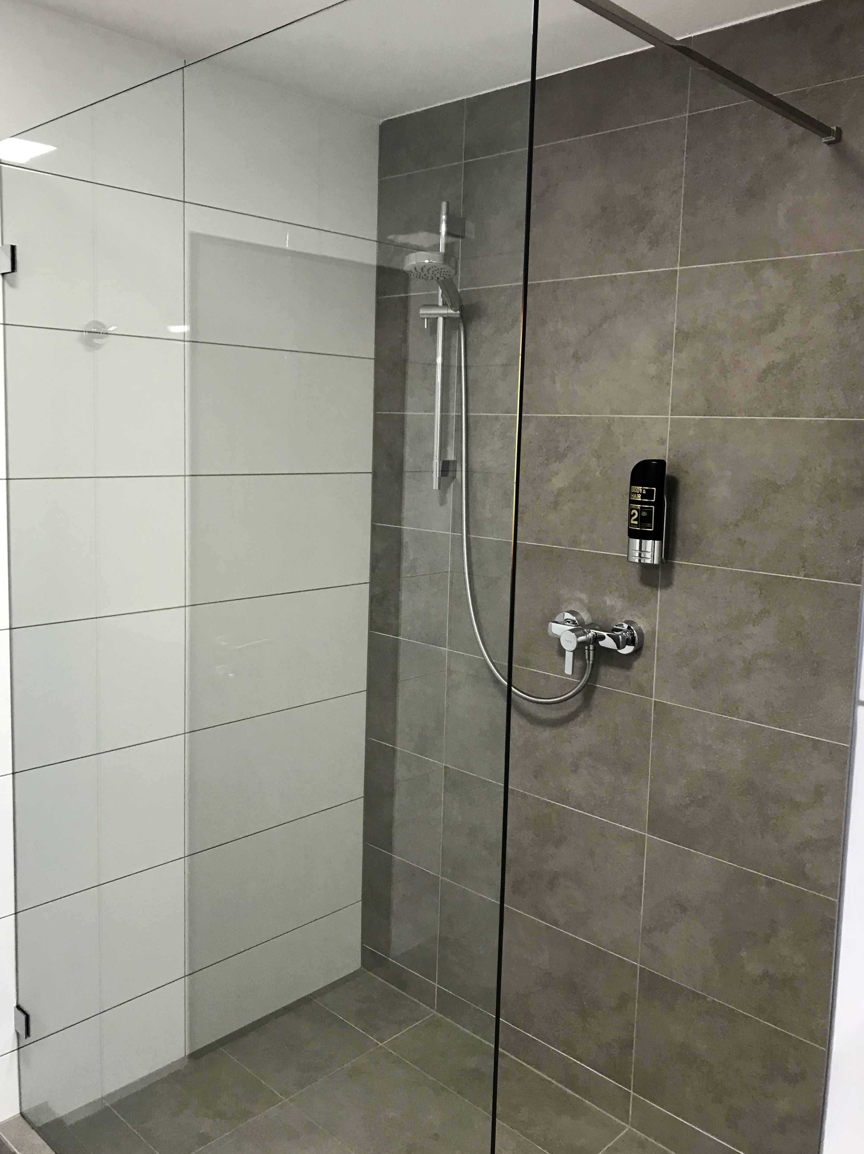 Een moderne douche met een digitaal display voor de temperatuur, een handdouche en een extra douchestraler.