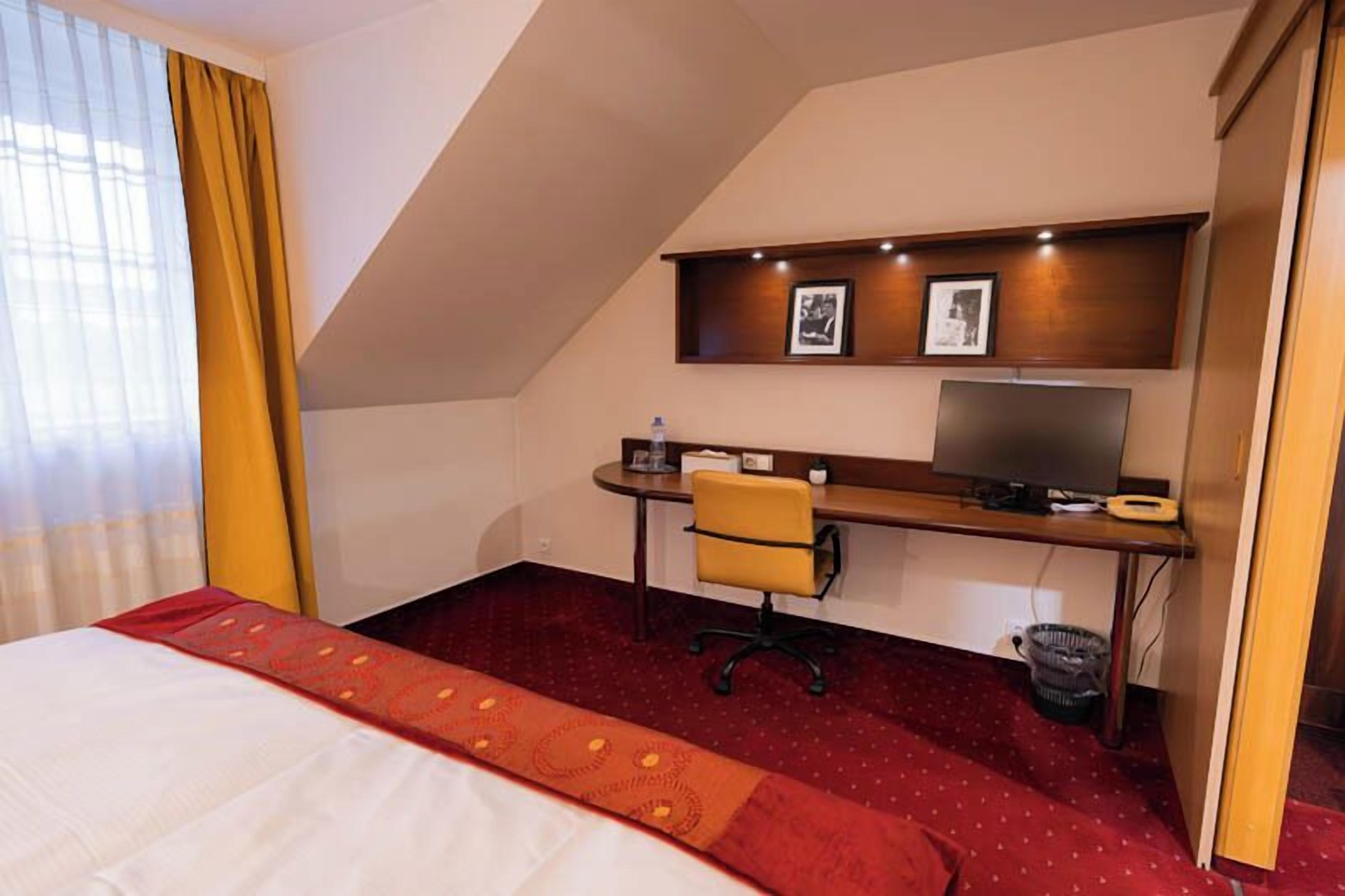 Ein Hotelzimmer mit einem Bett, einem Schreibtisch mit Stuhl, einem Fernseher und einem kleinen Regal mit Bildern.