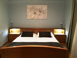 A neatly made bed with a wooden headboard, two bedside tables with lamps, and a floral painting on the wall.