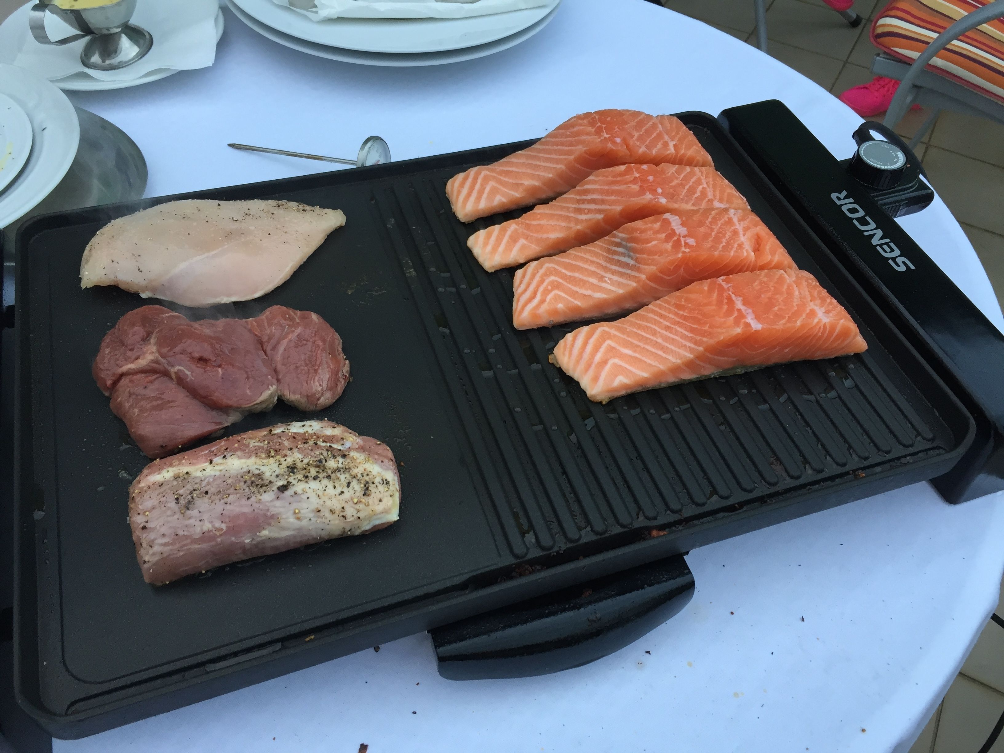 A grill with various meats and salmon on a white table.