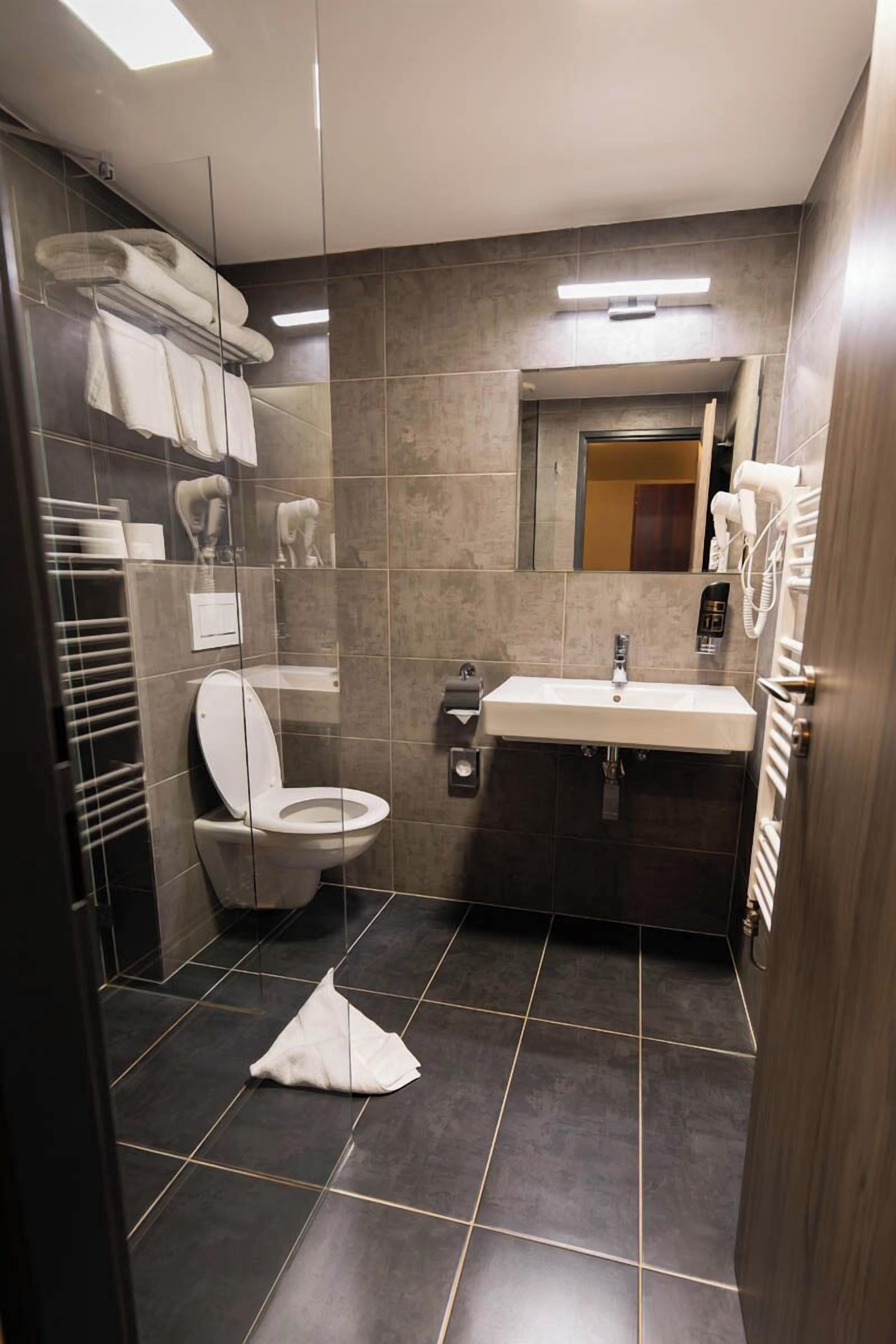 Un bagno moderno con box doccia in vetro, un water bianco, un lavandino con specchio sopra e un portasciuga con asciugamani piegati.