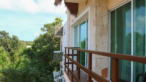 A balcony with a wooden railing overlooking lush greenery and a building with large windows. - Tulum Nah (Tulum)