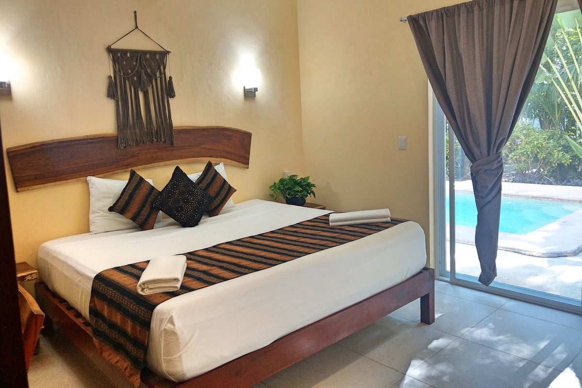 A neatly made bed with a striped bedspread, a wooden headboard, and a wall-mounted macrame decoration.