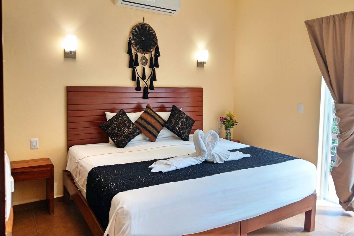 A neatly made bed with a wooden headboard, two wall-mounted lights, a dreamcatcher, and a vase with flowers.