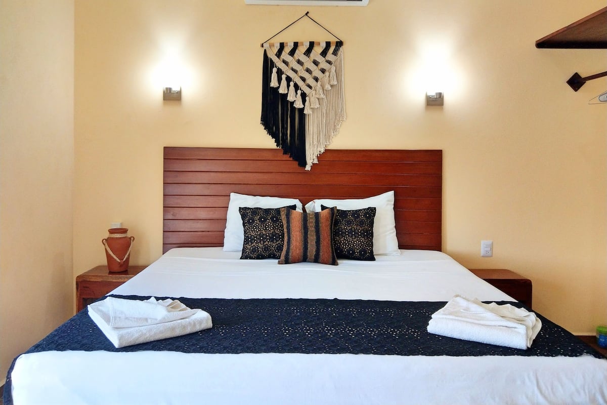 A neatly made bed with white linens, a dark blue throw blanket, and two white towels folded at the foot of the bed.