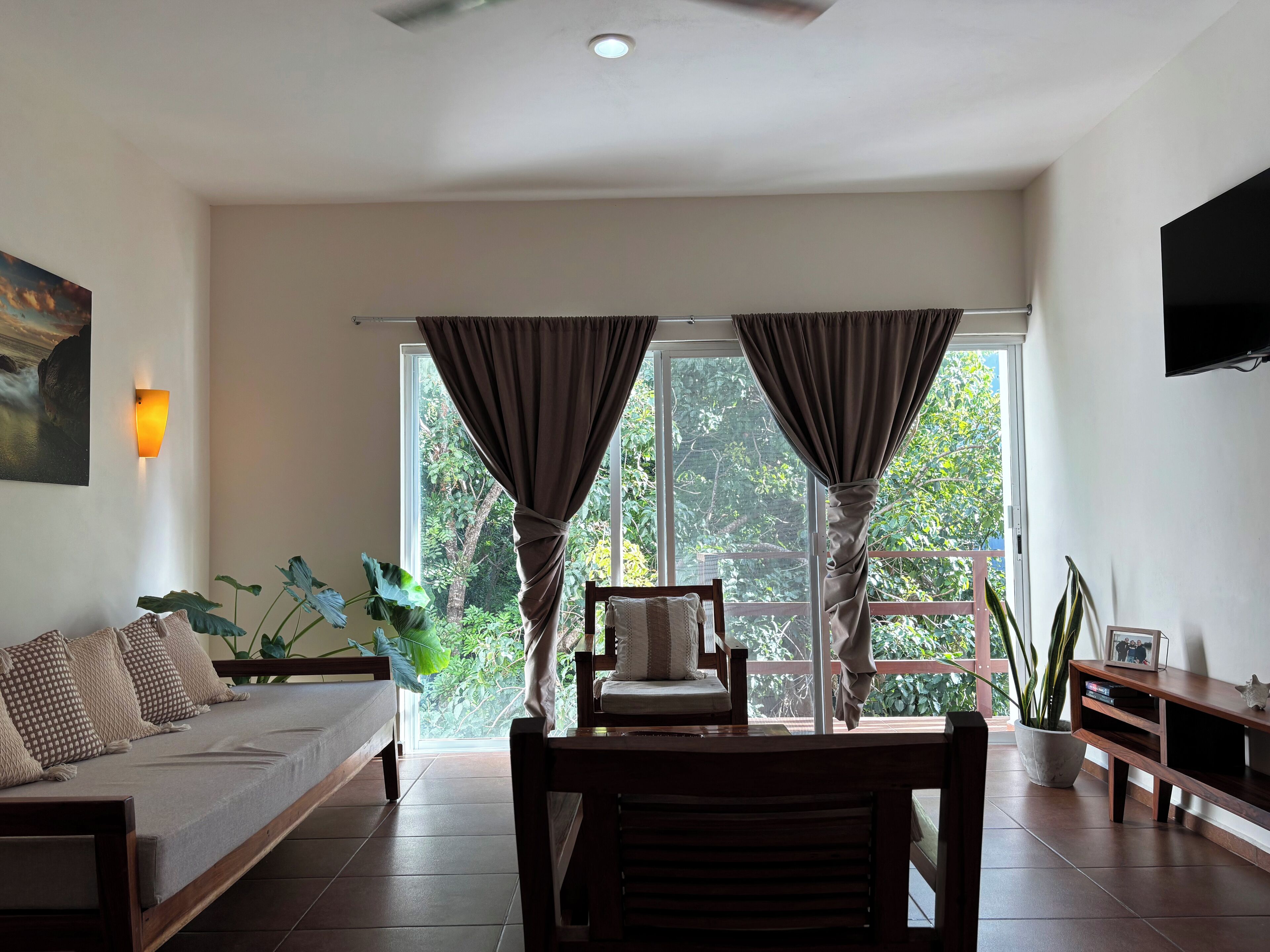 A living room with a sofa, a chair, a TV, and a large window with curtains.