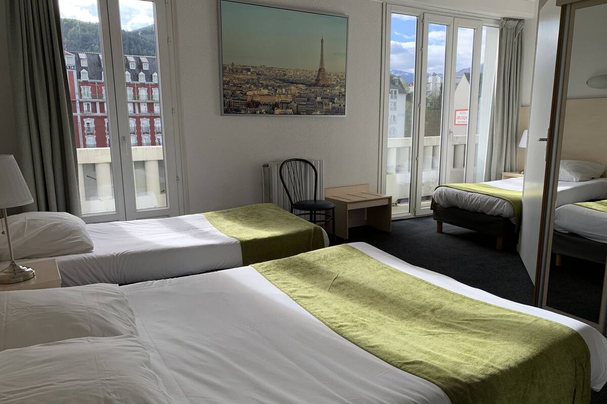 Een hotelkamer met twee bedden, een tafeltje, een stoel en een schilderij van een stadsgezicht.
