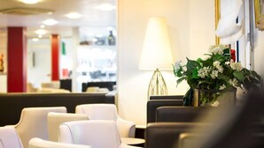 Un hall d’hôtel avec des fauteuils en cuir, une lampe et un vase de fleurs.