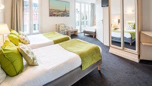 Une chambre d’hôtel avec deux lits, un bureau, une chaise, une télévision et une grande fenêtre donnant sur le paysage urbain.