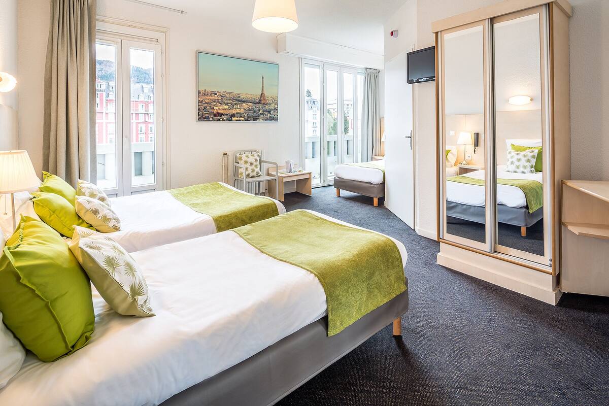 Hotelkamer met twee bedden, een bureau, een stoel, een televisie en een groot raam met uitzicht op de stad.