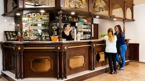 A bar area with a wooden counter, shelves with bottles, and a tiled floor. - Hôtel Hélianthe (Lourdes)