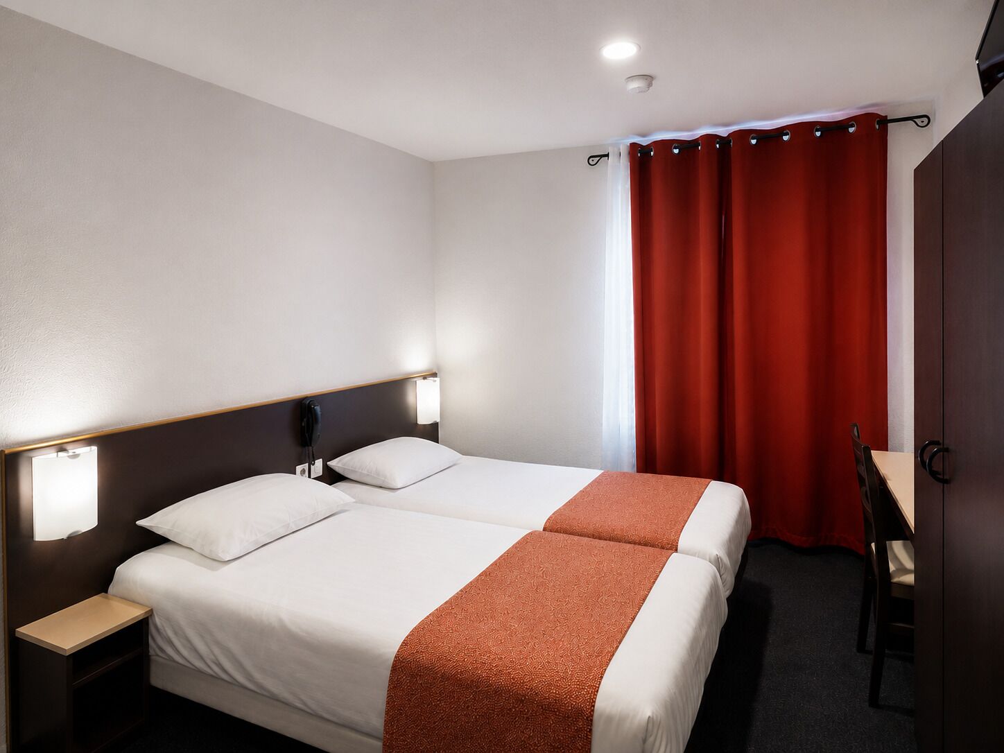 Una habitación de hotel con una cama doble, mesitas de noche, un escritorio y una silla.