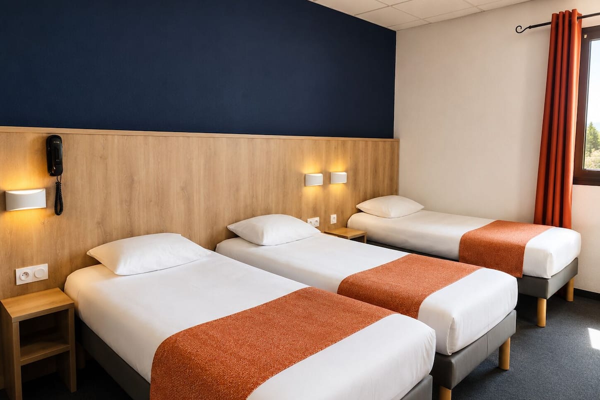 A hotel room with two beds, a wooden headboard, bedside lamps, a phone, and a window with curtains.