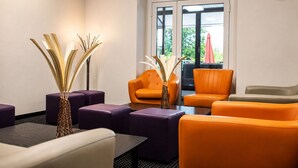 A modern lounge area with purple and orange seating, a large window, and a decorative wall clock. - Hôtel Hélianthe (Lourdes)