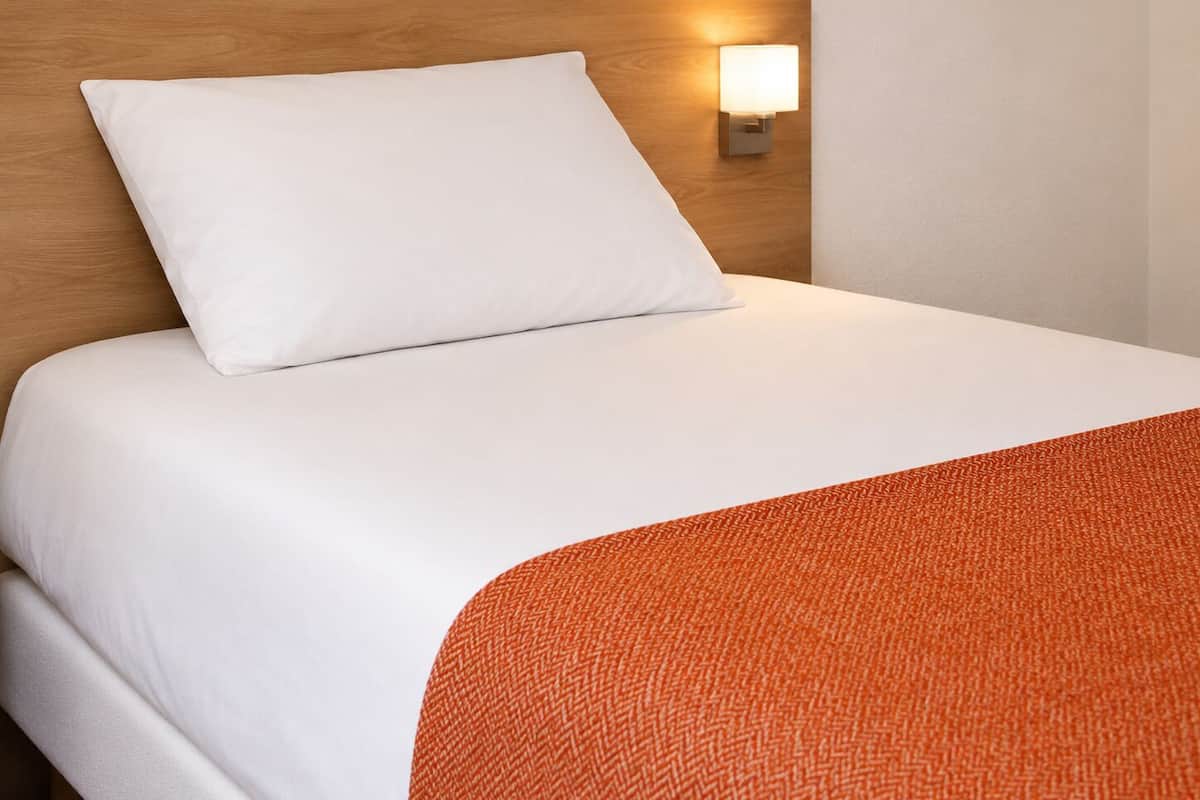 A neatly made bed with a white pillow and an orange textured blanket.