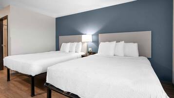 Habitación de hotel con dos camas, una mesita de noche con lámpara y una puerta a la izquierda.